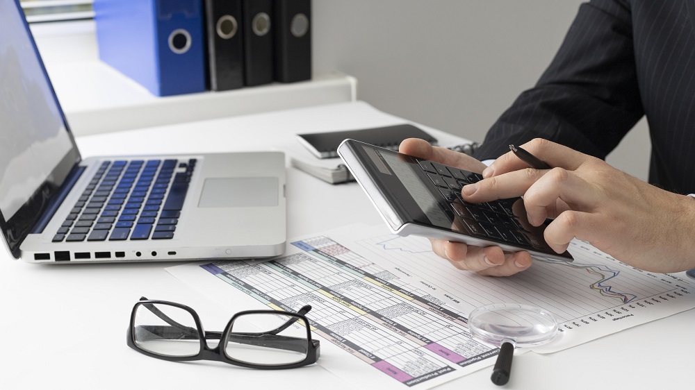 Homem próximo a um óculos e a uma calculadora fazendo cálculos representando a redução de custos para 